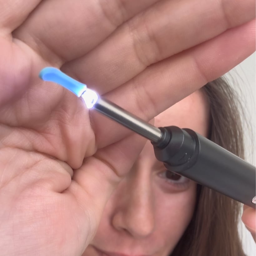 Person holding a lit dental curing light close to their face.